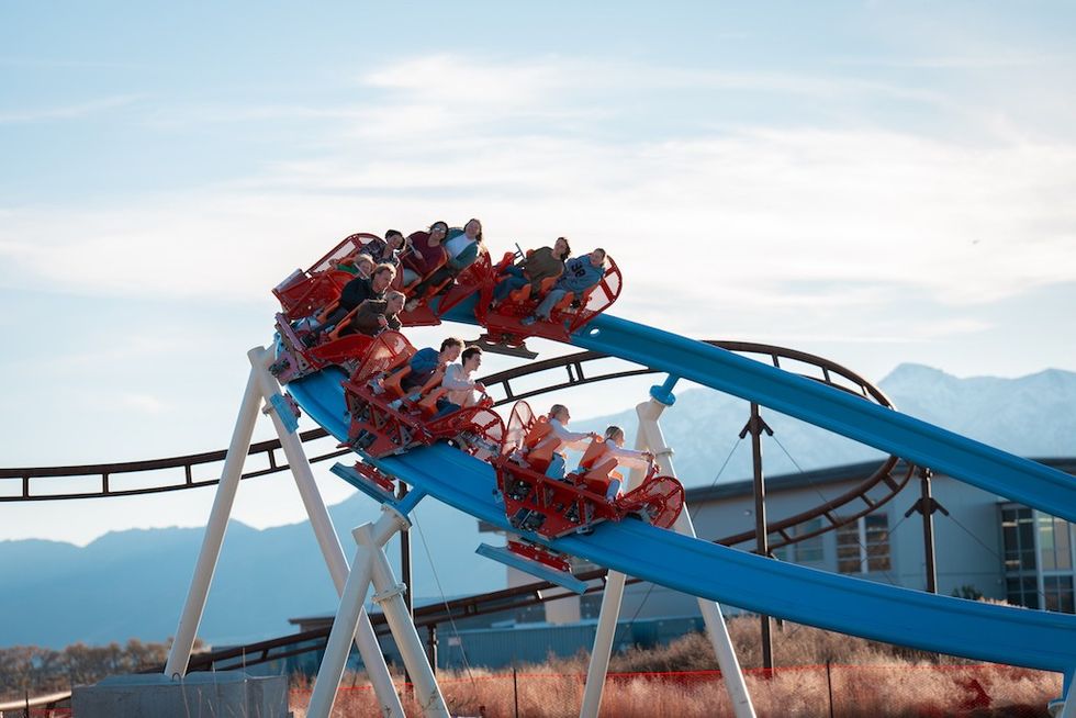 People on a blue roller coaster with snowy mountains in the background.
