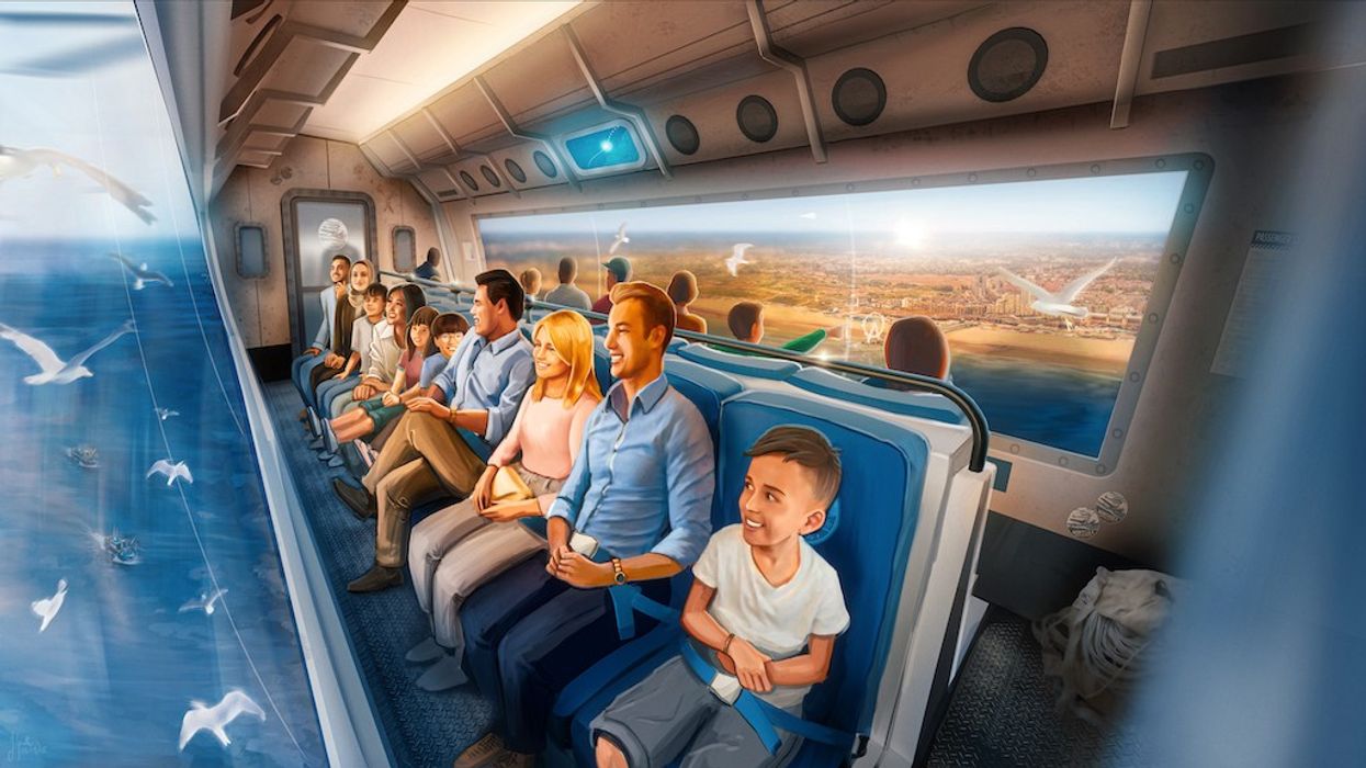 People on a motion ride with large windows overlooking an ocean and cityscape, surrounded by birds.