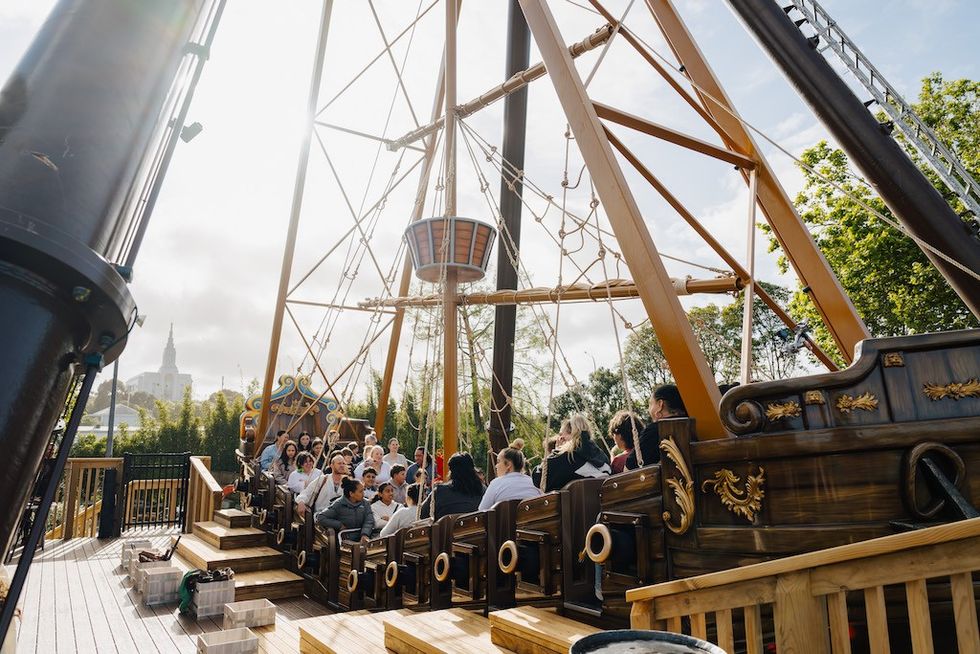 People on a swinging pirate ship ride at an amusement park under a cloudy sky.