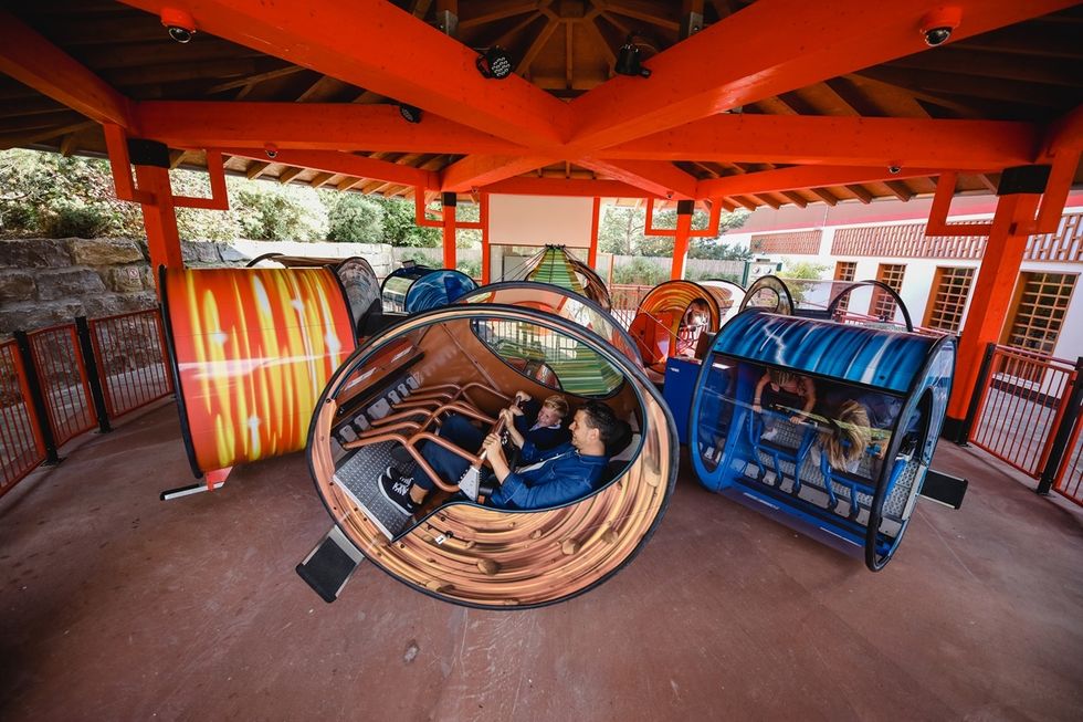 People on a wooden-themed spinning ride named the Loopster, under a wooden shelter with bright orange beams.