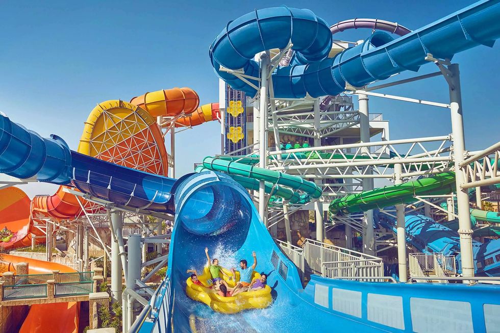 People on a yellow raft slide down a curved blue water slide at a vibrant water park, Aquaventure World