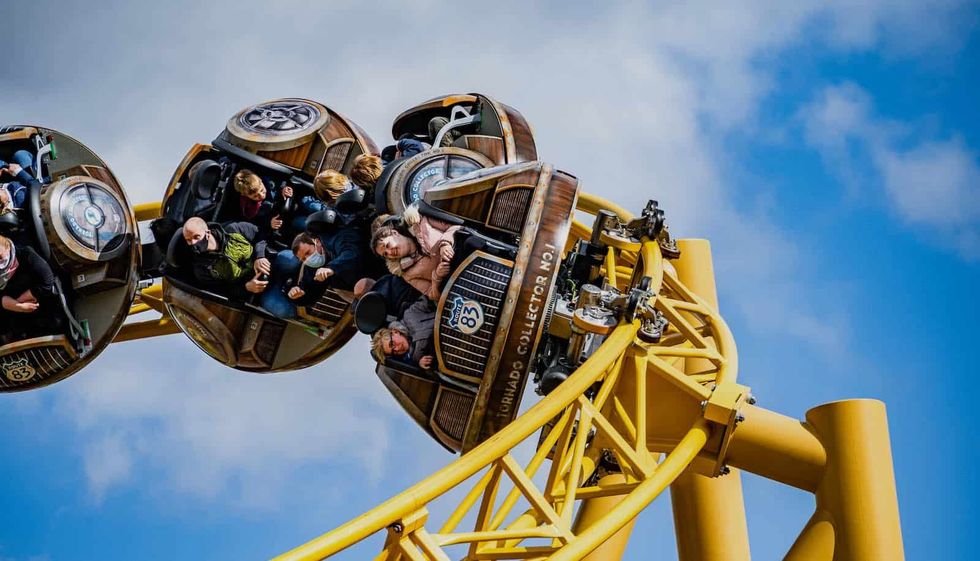People on a yellow roller coaster with spinning carriages under a blue, cloudy sky.