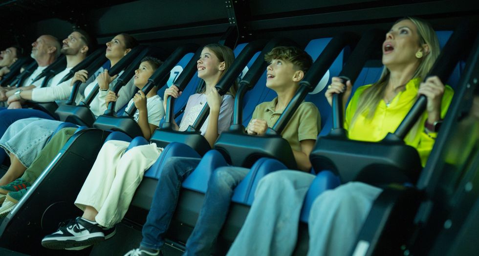 People on an amusement ride, sitting in seats with safety bars, looking excited and amazed.