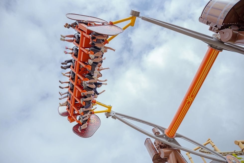 People on an orange thrill ride, Vild Swing, spinning upside down against a cloudy sky.