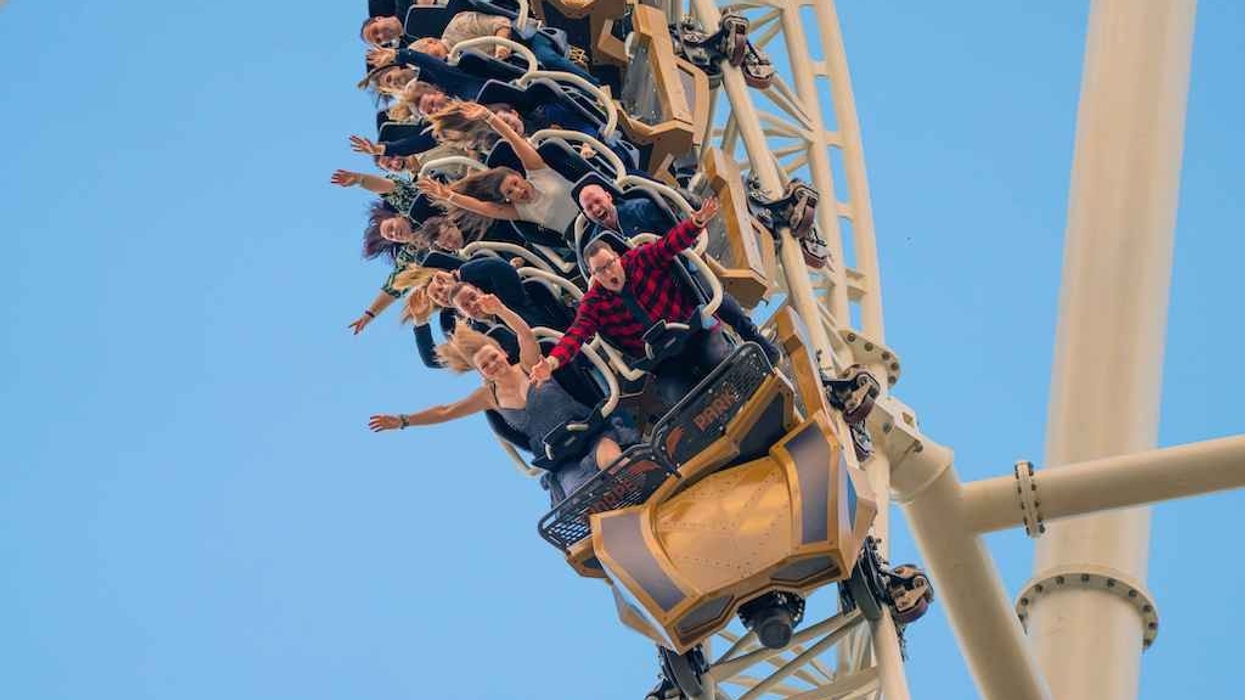 People on Hyperia roller coaster descending steeply, arms raised, against a clear blue sky.