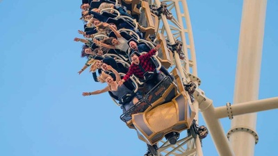 People on Hyperia roller coaster descending steeply, arms raised, against a clear blue sky.