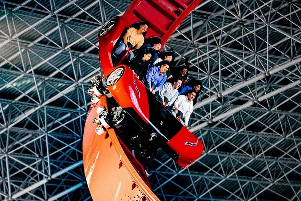 People on Mission Ferrari roller coaster shaped like a red car, on a steep indoor curve.