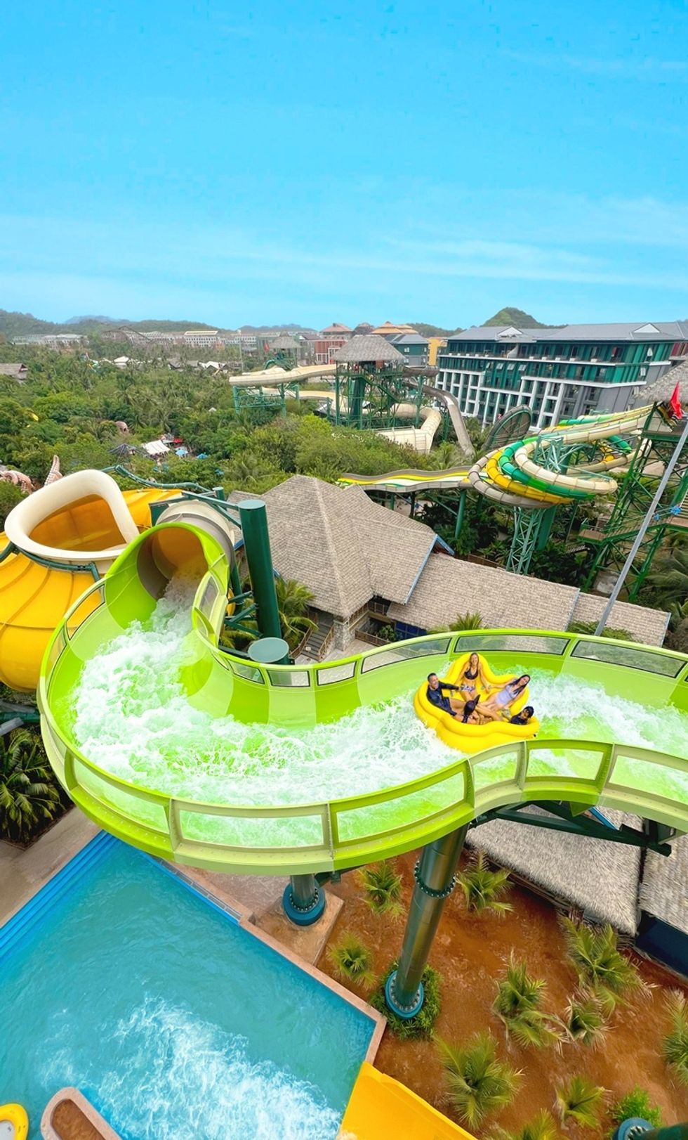 People on PowerRAPIDS ride a yellow raft sliding down a green water slide in an amusement park.