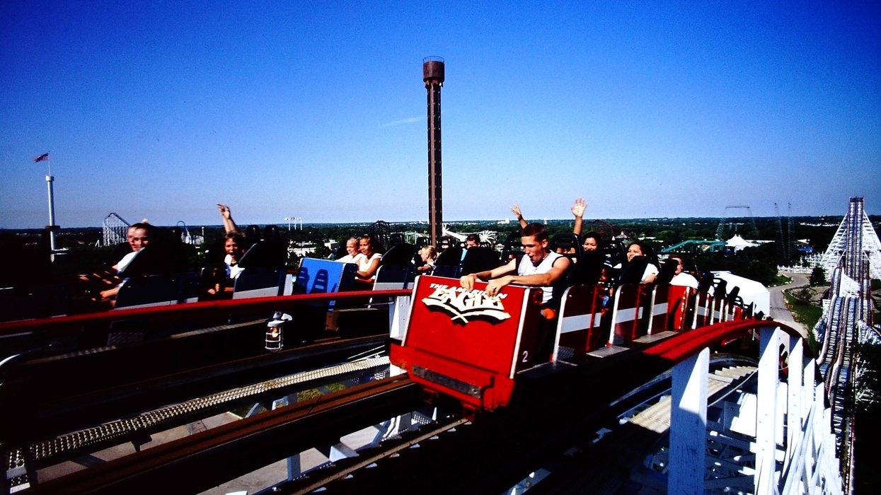 People on the red and blue American Eagle roller coaster at Six Flags Great America, arms raised, against a clear blue sky.