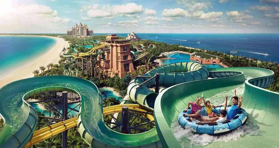 People on waterslide raft at a beachside waterpark, with sea view and resort in background.