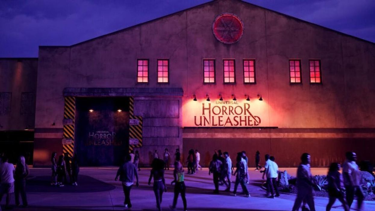 People outside a lit-up attraction labeled "Horror Unleashed" at night.