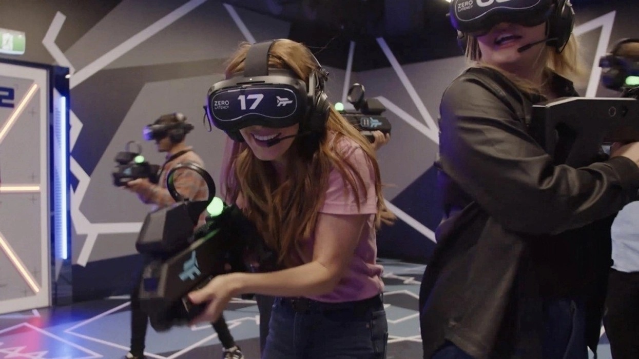 People playing a Zero Latency VR game in a futuristic room, wearing headsets and holding controllers.