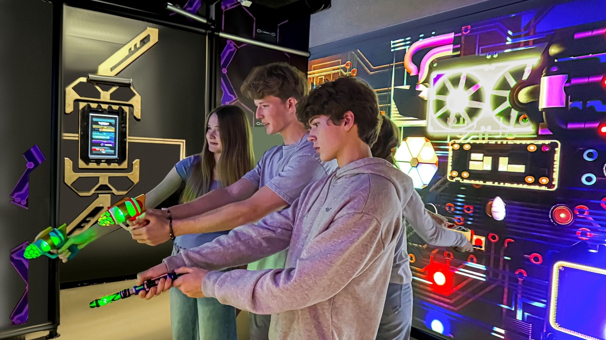 People playing an interactive laser tag game with neon lights on a futuristic wall.