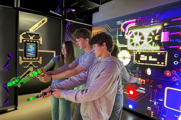 People playing an interactive laser tag game with neon lights on a futuristic wall.