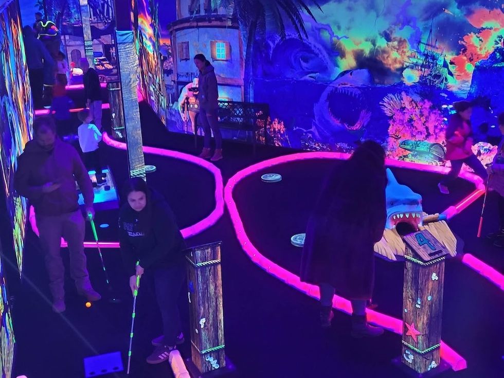 People playing glow-in-the-dark mini-golf with neon undersea-themed decor.