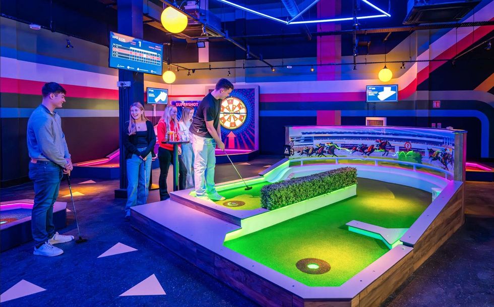 People playing indoor mini golf from 360Golf in a vibrant, neon-lit setting.
