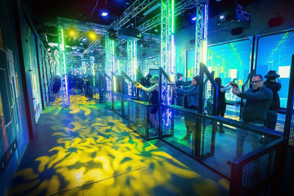 People playing laser tag in a neon-lit arena with vibrant colors and digital visuals.