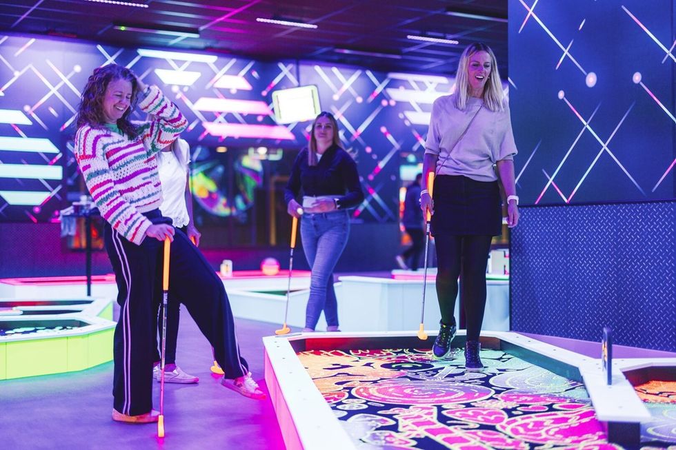 People playing neon-lit mini golf from 360Golf indoors, laughing and enjoying.