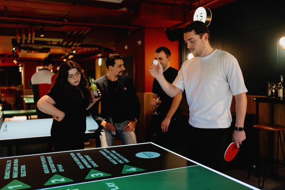 People playing ping pong and socializing in a lively bar setting.
