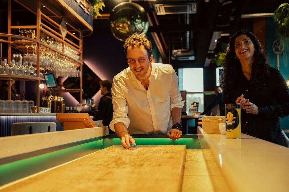 People playing shuffleboard in a lively bar setting.