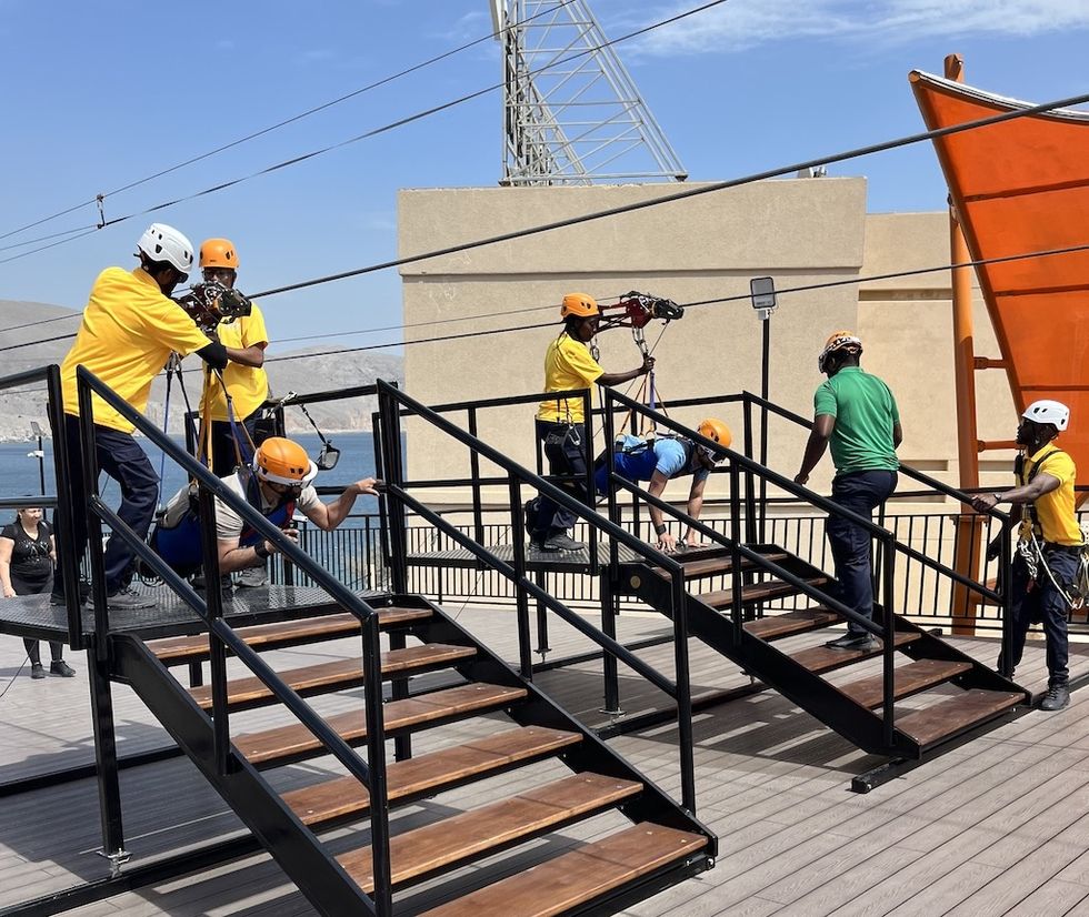 People preparing for a ziplining activity on a platform with safety helmets and harnesses.