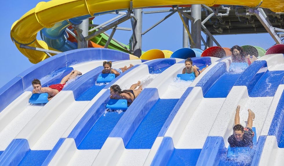 People racing down colorful multi-lane water slides on blue mats at Typhoon Texas