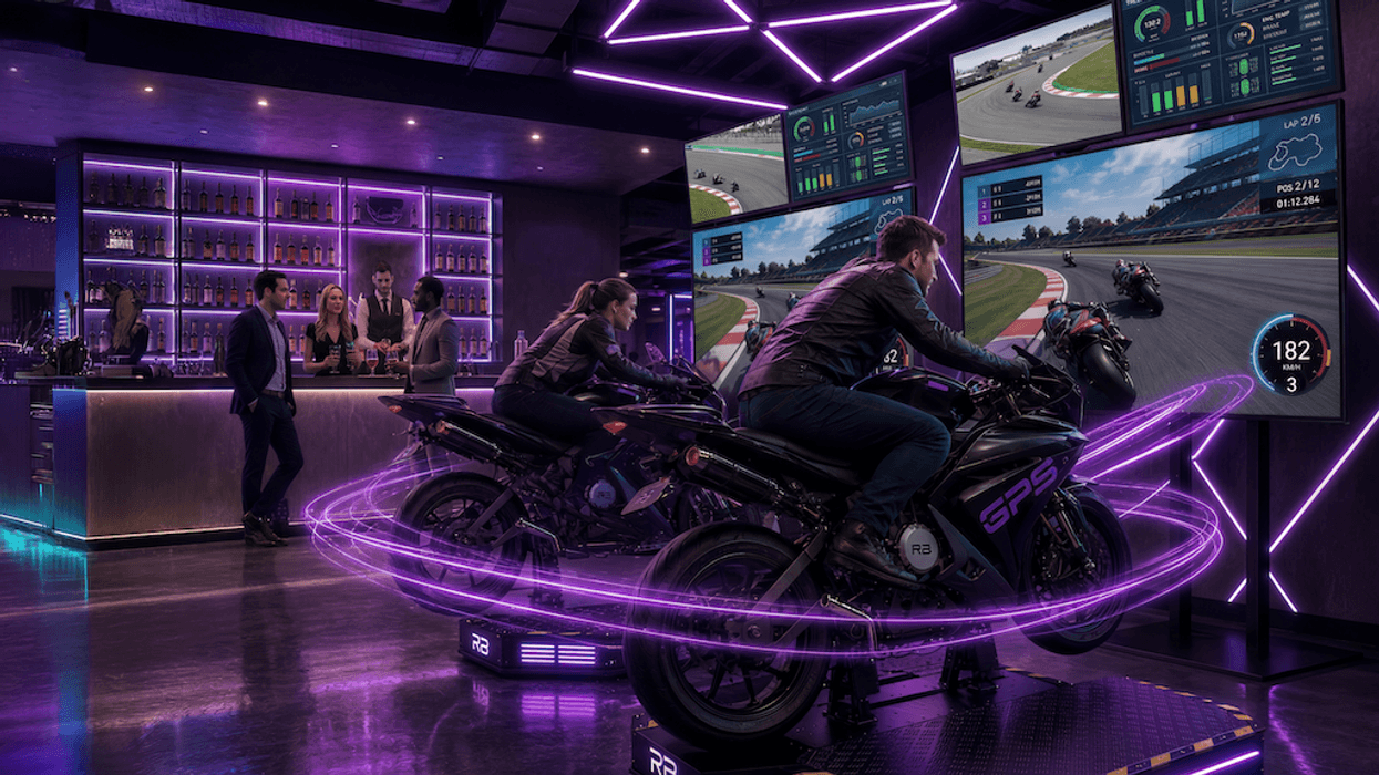 People racing motorcycles in a neon-lit simulator with spectators at a bar.