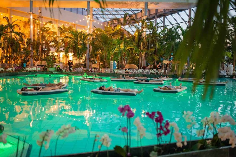 People relaxing on floating mats in an indoor pool surrounded by tropical plants at Suntago Water World.