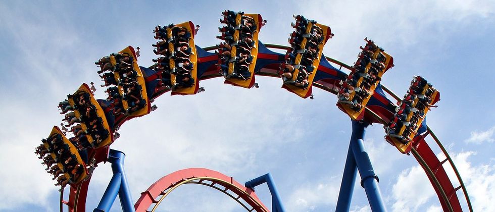 People riding a colorful roller coaster upside down against a blue sky.