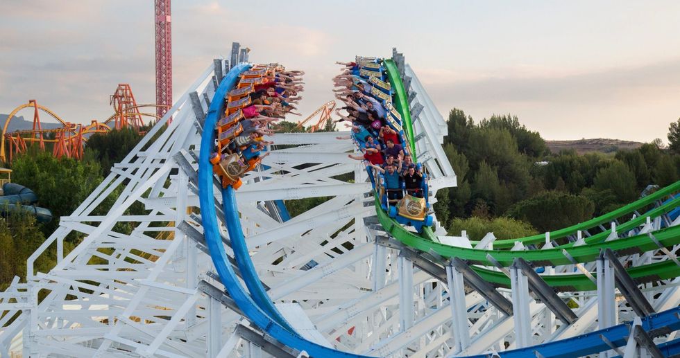 People riding a colorful, twisting roller coaster with arms raised, surrounded by trees.