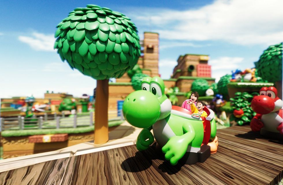 People riding a green dinosaur-themed ride called Yoshi's Adventure in a colorful amusement park called Super Nintendo World