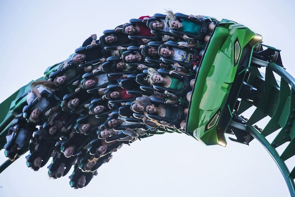 People riding a green roller coaster upside down, with excited and surprised expressions.