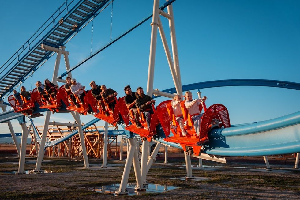 People riding a red and blue roller coaster under a clear blue sky.
