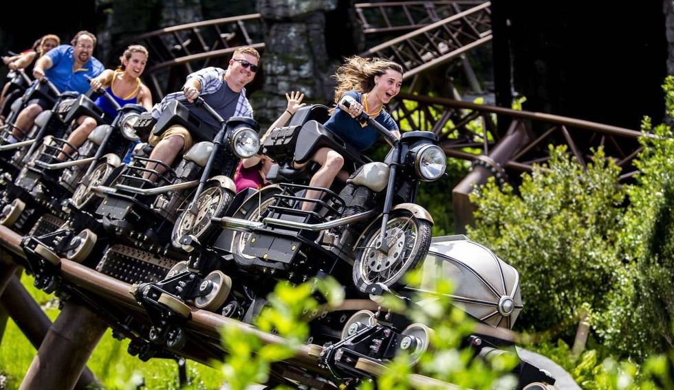 People riding a roller coaster designed as motorcycles, surrounded by greenery.