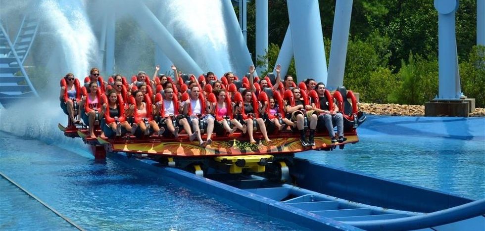 People riding a roller coaster over water, creating a splash.