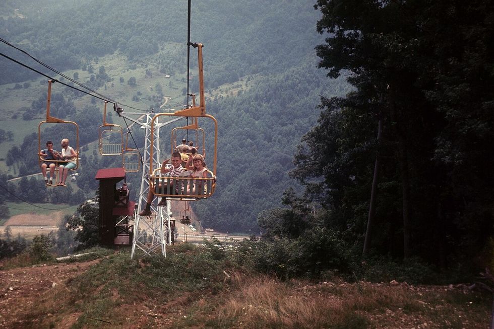 People riding a ski lift over a scenic, forested mountain landscape on the way to Ghost Town in the Sky theme park