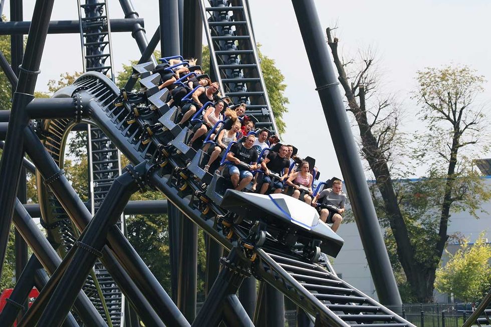 People riding a steel roller coaster, Hyperion, descending a steep drop in Energylandia theme park.
