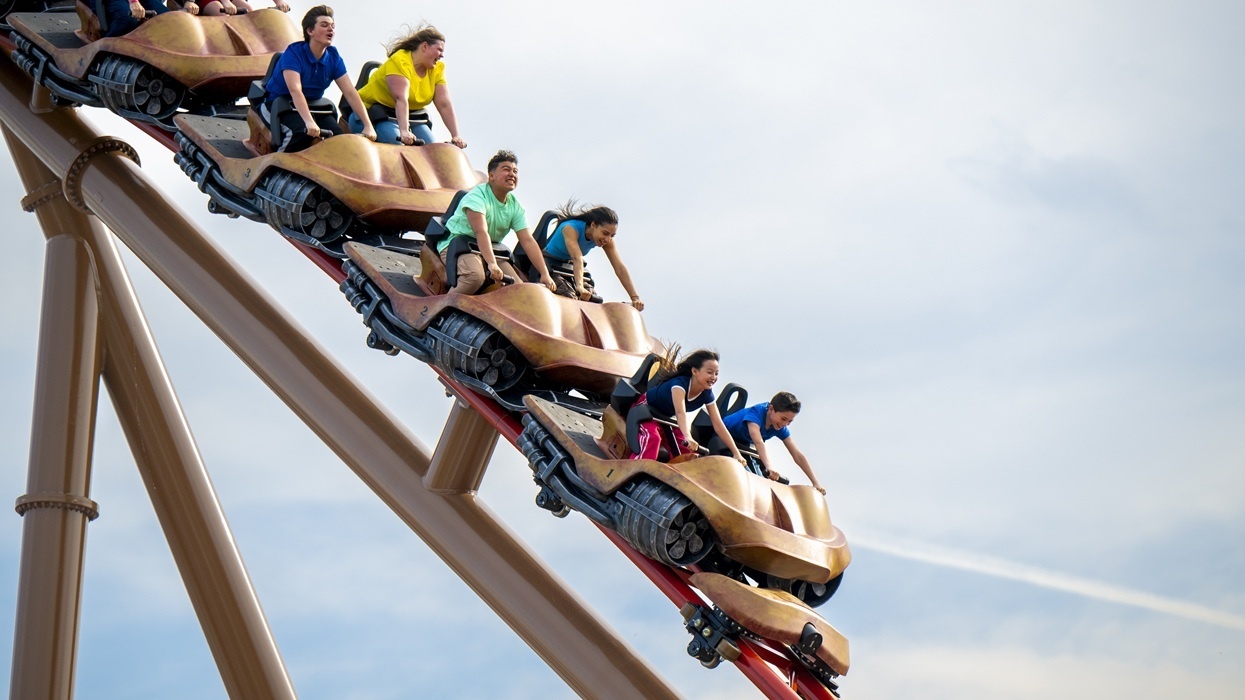 People riding a steep roller coaster drop under a slightly cloudy sky.