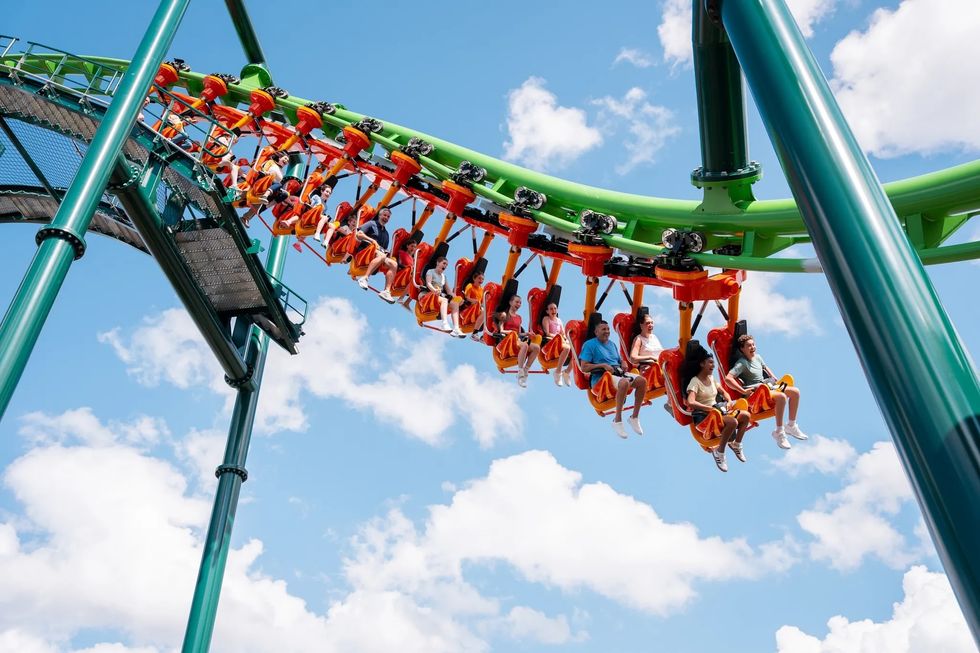 People riding a suspended roller coaster called Flying Fox against a blue sky with clouds at Kentucky Kingdom.