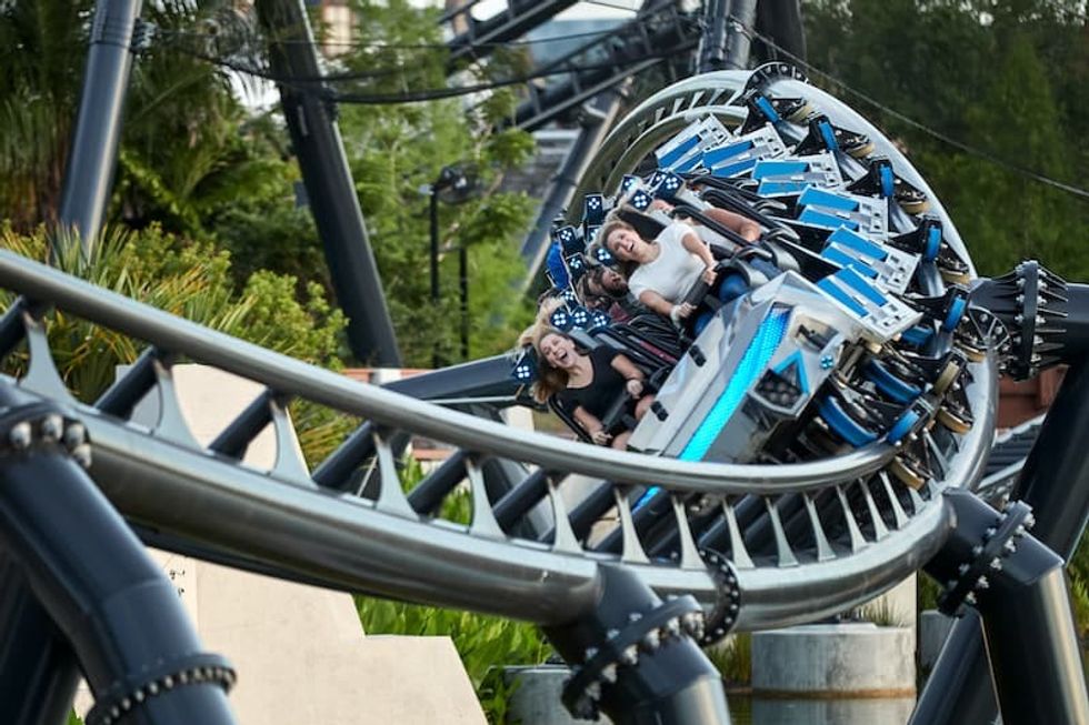 People riding a twisting roller coaster (VelociCoaster) through a lush, green setting.
