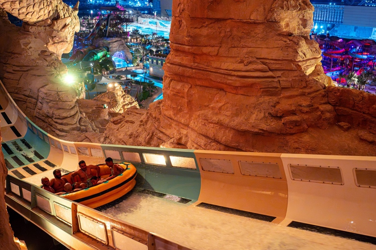 People riding a water slide at night in a rocky, illuminated water park named Aquarabia