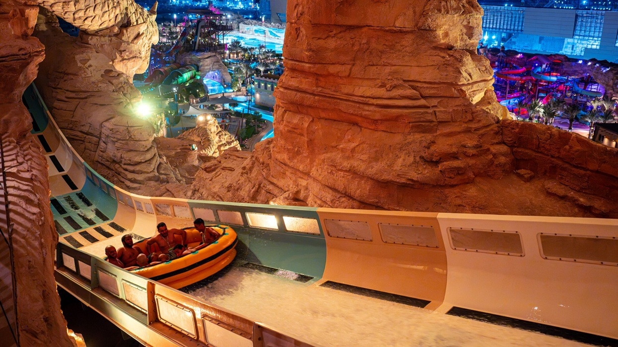 People riding a water slide at night in a rocky, illuminated water park named Aquarabia