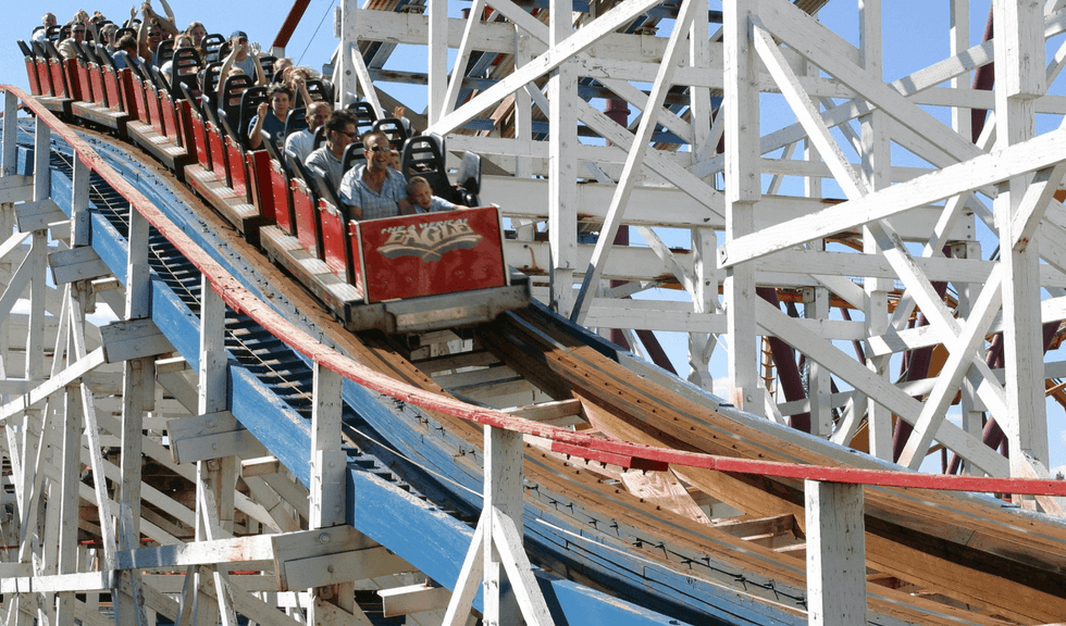 People riding a wooden roller coaster called American Eagle at Six Flags Great America with red and blue tracks.