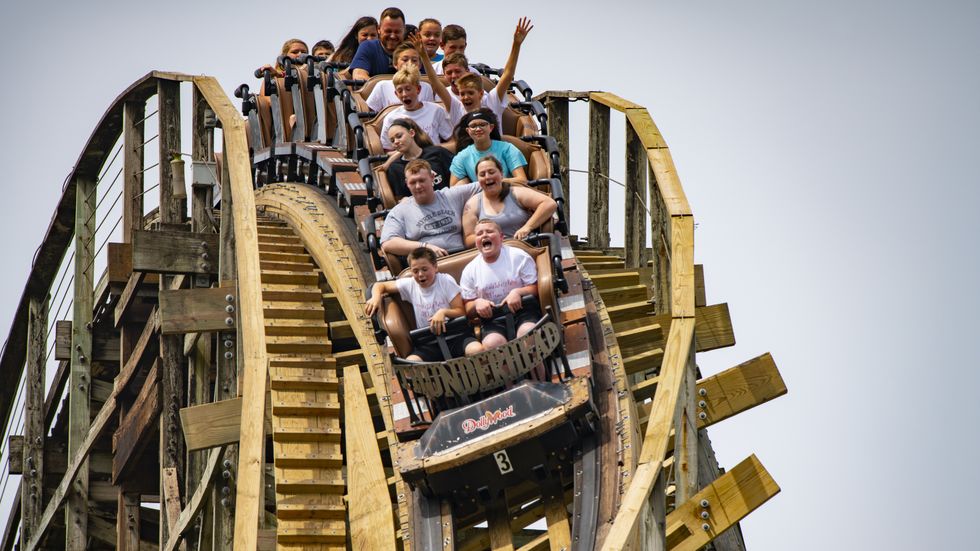 People riding a wooden roller coaster, some smiling, others screaming.