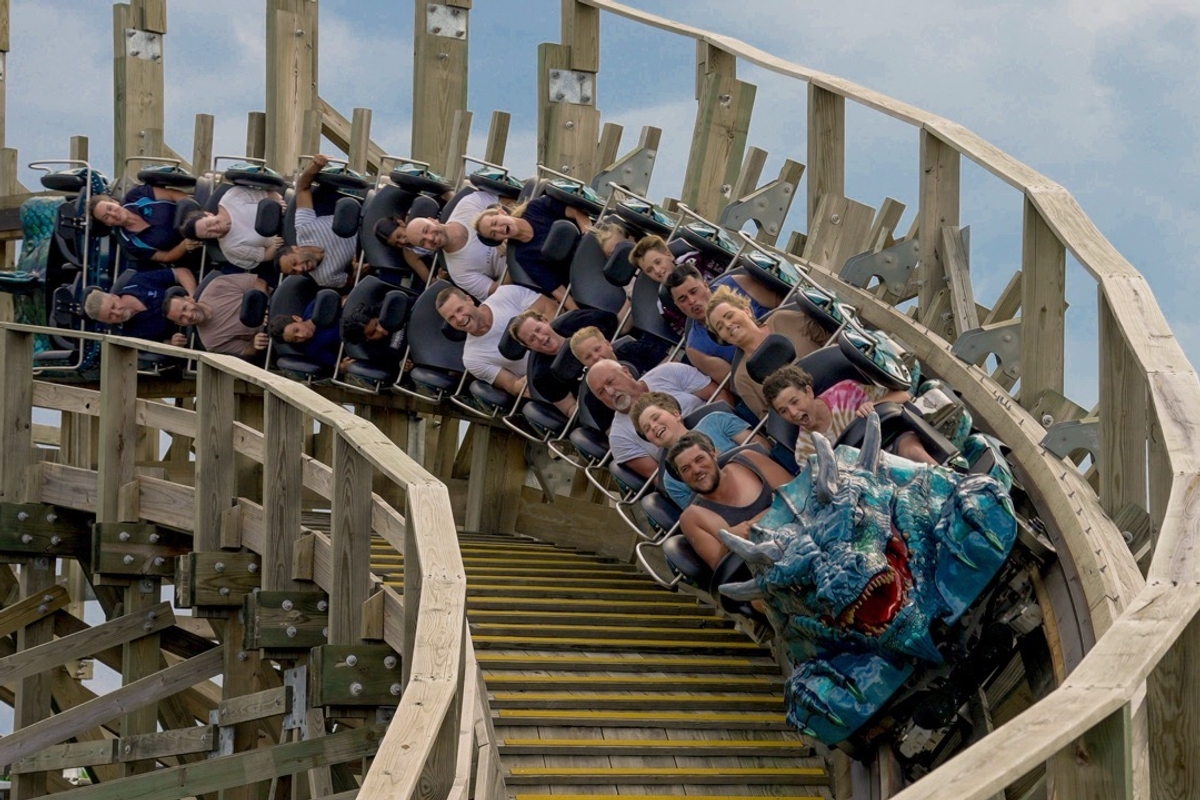 People riding a wooden roller coaster with a blue dragon-themed front.