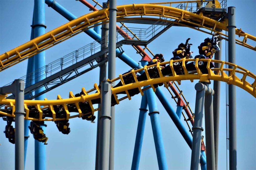 People riding a yellow roller coaster with blue supports against a clear sky.