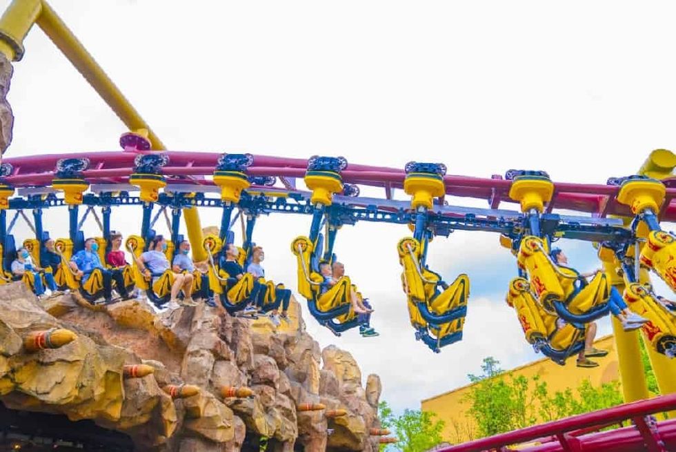 People riding an inverted roller coaster over rocky terrain at Fantawild Dino Kingdom