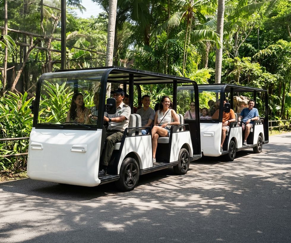 People riding an open-air electric tram through a lush, tropical setting.