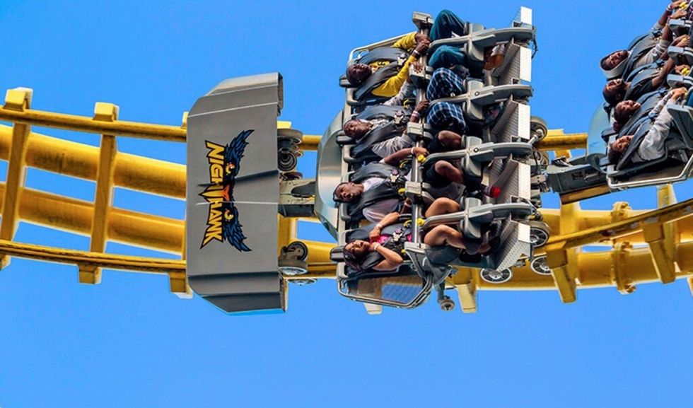 People riding the Nighthawk roller coaster upside down against a clear blue sky.