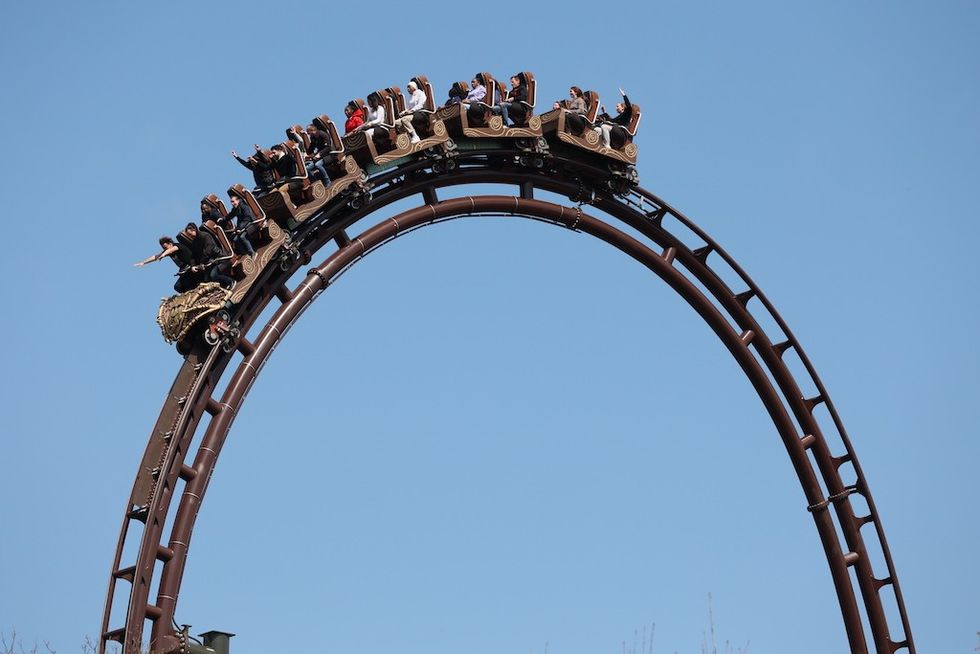 People riding Toutatis roller coaster at Parc Asterix upside down against a clear blue sky.